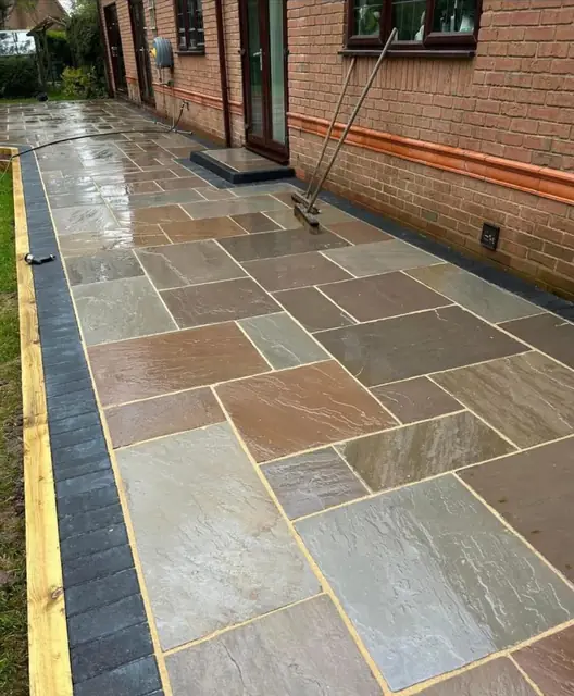Sandstone paving with a dark border running alongside a brick wall