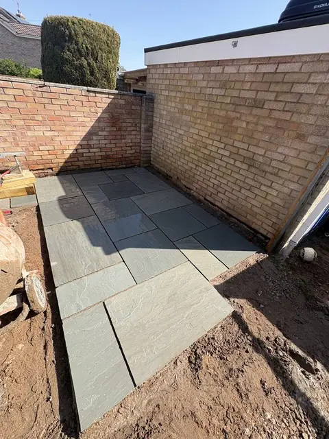 A dark grey porcelain patio laid against a brick wall