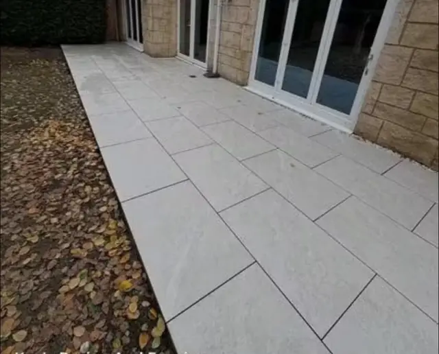 Pale porcelain paving laid against a stone faced house