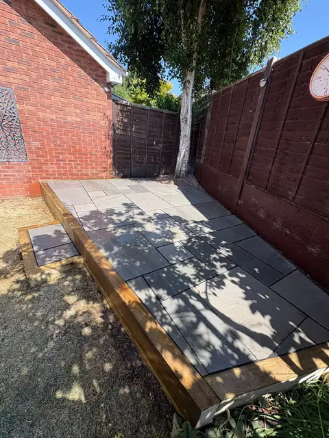 A raised sandstone patio with black border slabs and timber steps