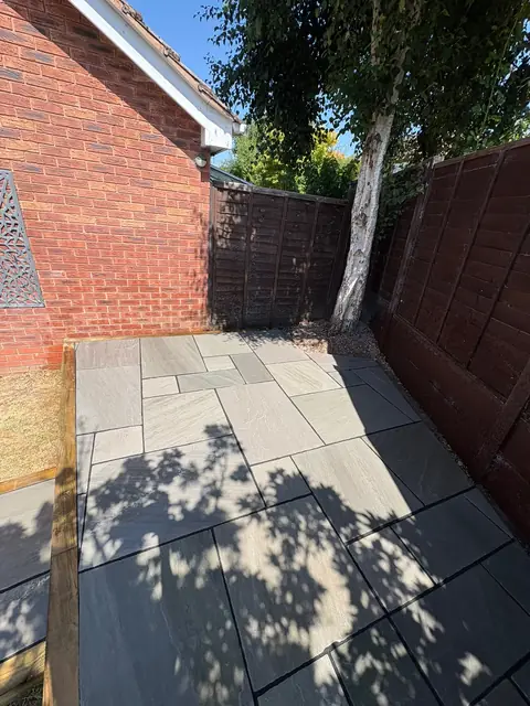 A grey and black patio finished with sleeper edging under a tree