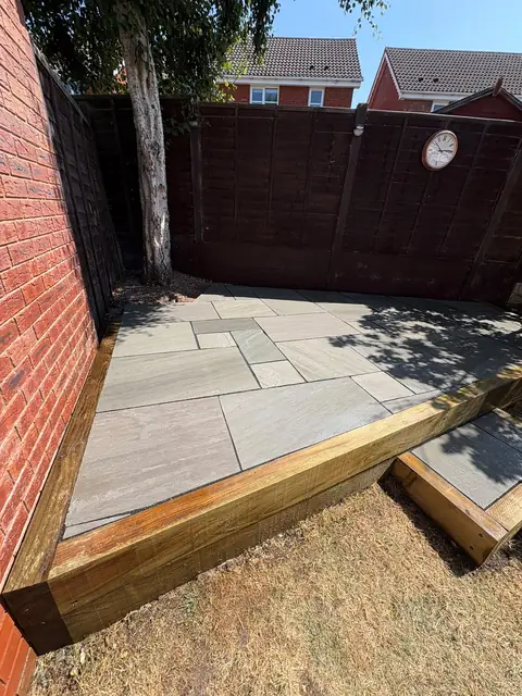 A raised sandstone patio with a timber planter along one side